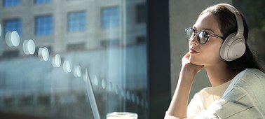    A female in a cafe wearing Sony WH-1000XM3 Headphones, immersed in the music